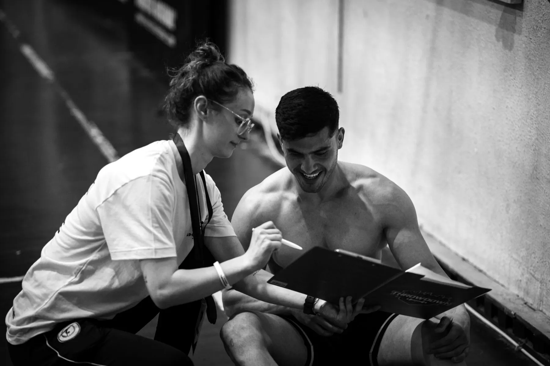 A coach going through a plan on a clipboard with a client in the gym, black and white